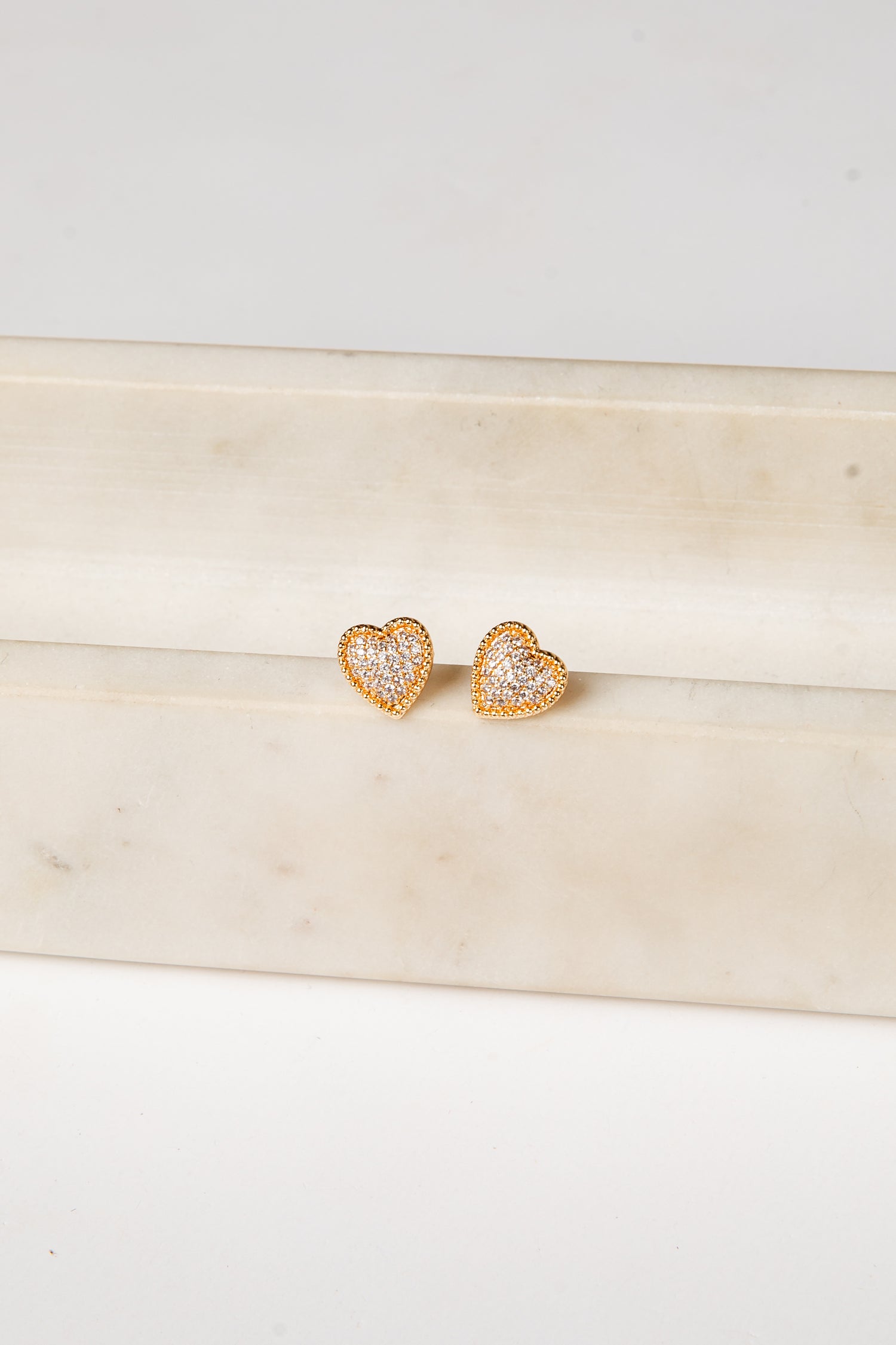 Heart-shaped earrings with clear stones on a light wooden surface