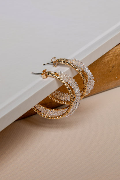 Gold hoop earrings with clear gemstones on a beige surface