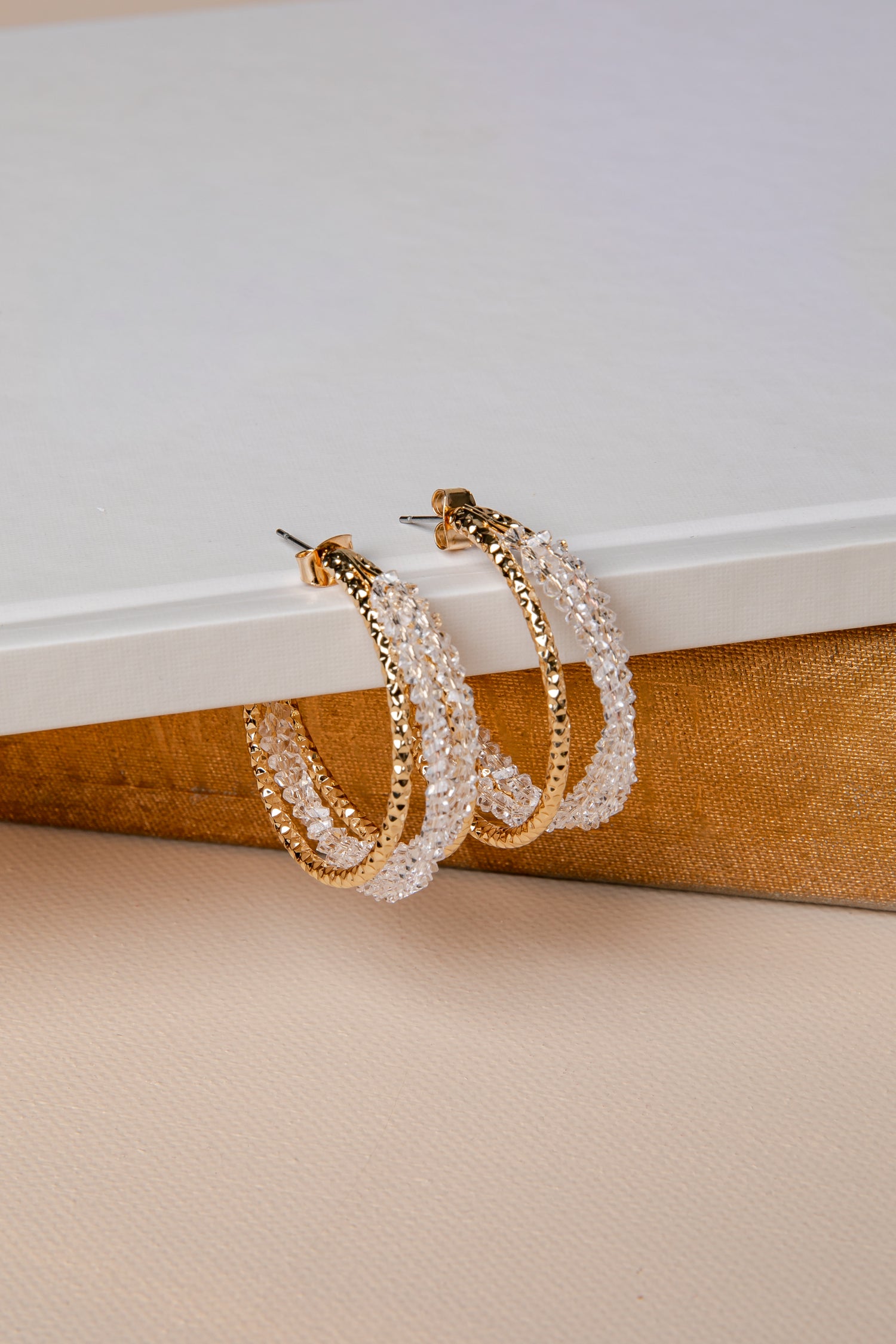 Pair of gold and pearl hoop earrings on a textured surface with a neutral background