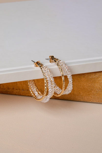 Pair of gold and pearl hoop earrings on a textured surface with a neutral background