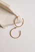 A pair of textured gold hoop earrings displayed on a light beige stone slab against a clean off-white background.