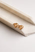 A pair of small gold knot stud earrings resting on a cream-colored stone tray against a white background.