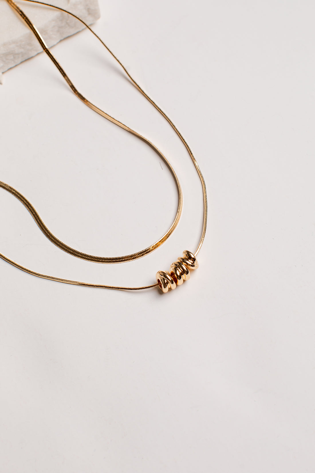 A gold-toned double-strand necklace featuring a textured, coiled bead pendant, displayed on a clean white surface.