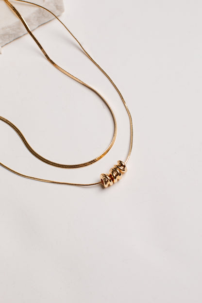 A gold-toned double-strand necklace featuring a textured, coiled bead pendant, displayed on a clean white surface.