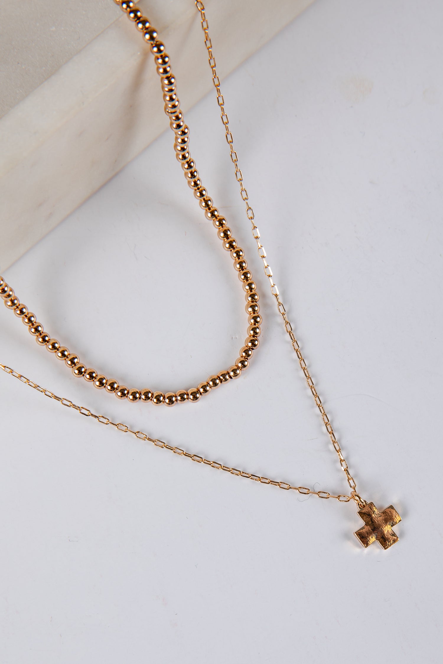 Two gold necklaces with a cross pendant on a light background