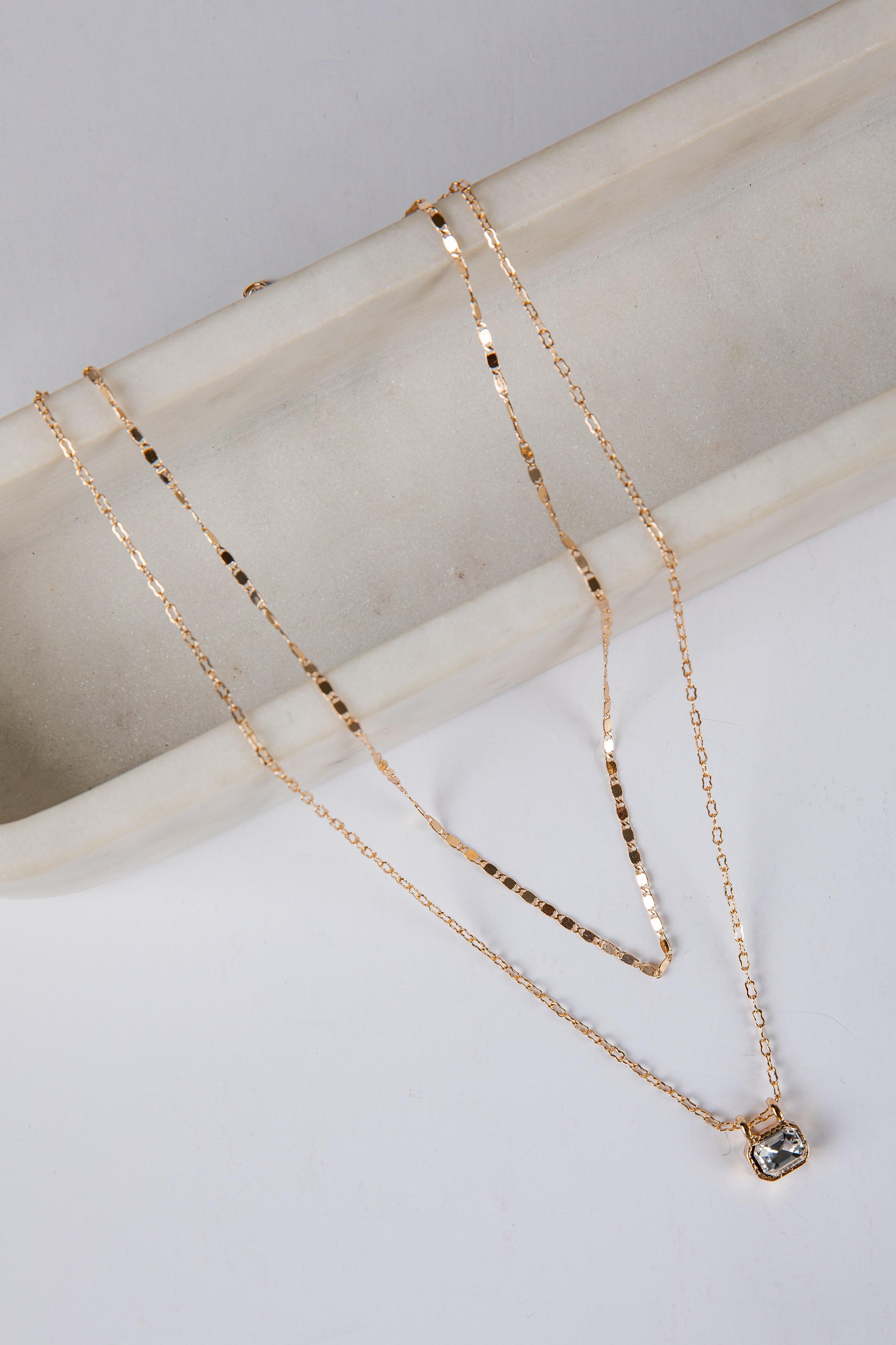 Two gold necklaces on a light gray surface