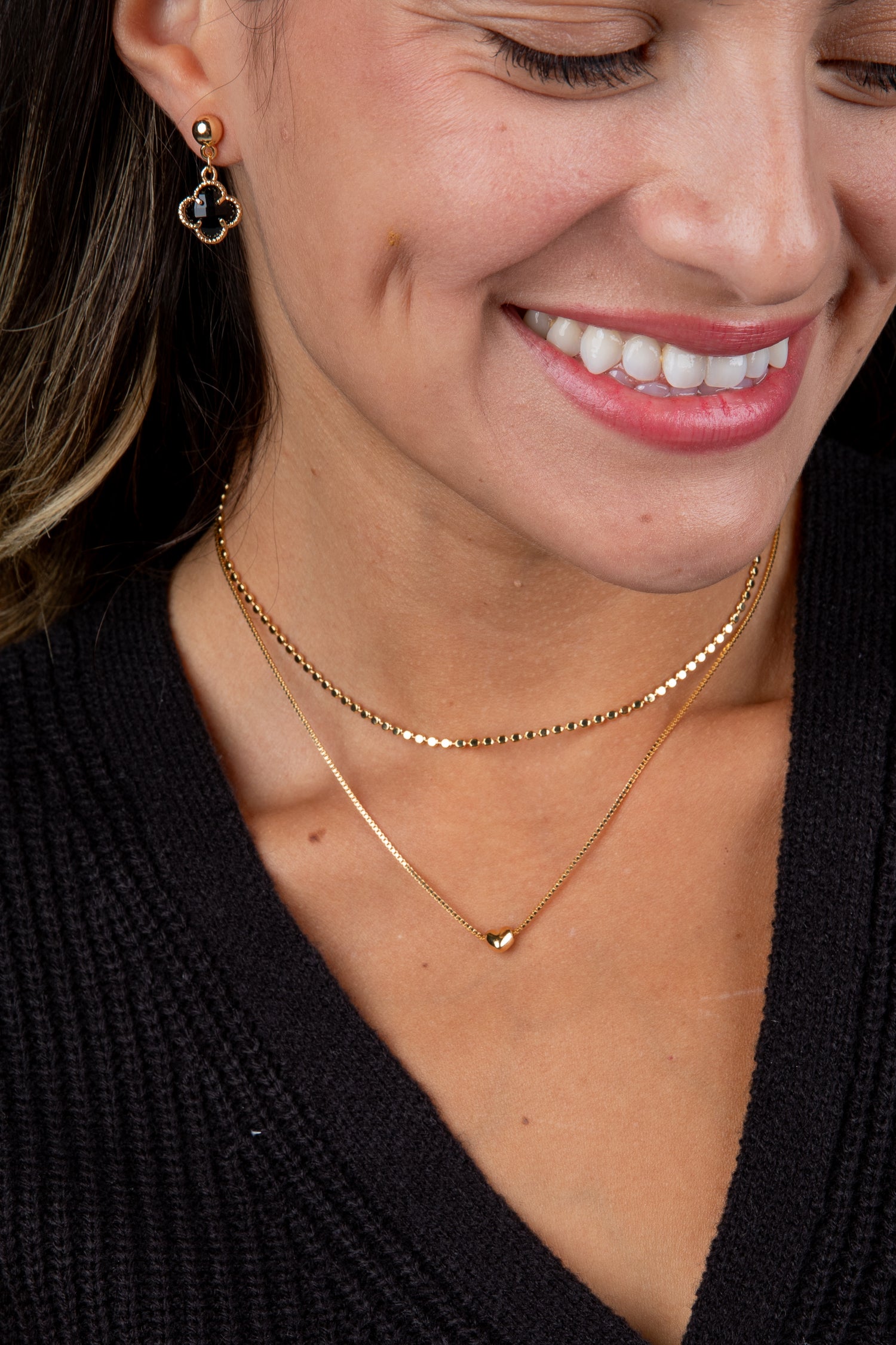 Close-up of a woman wearing gold necklaces and earrings, with a blurred background.