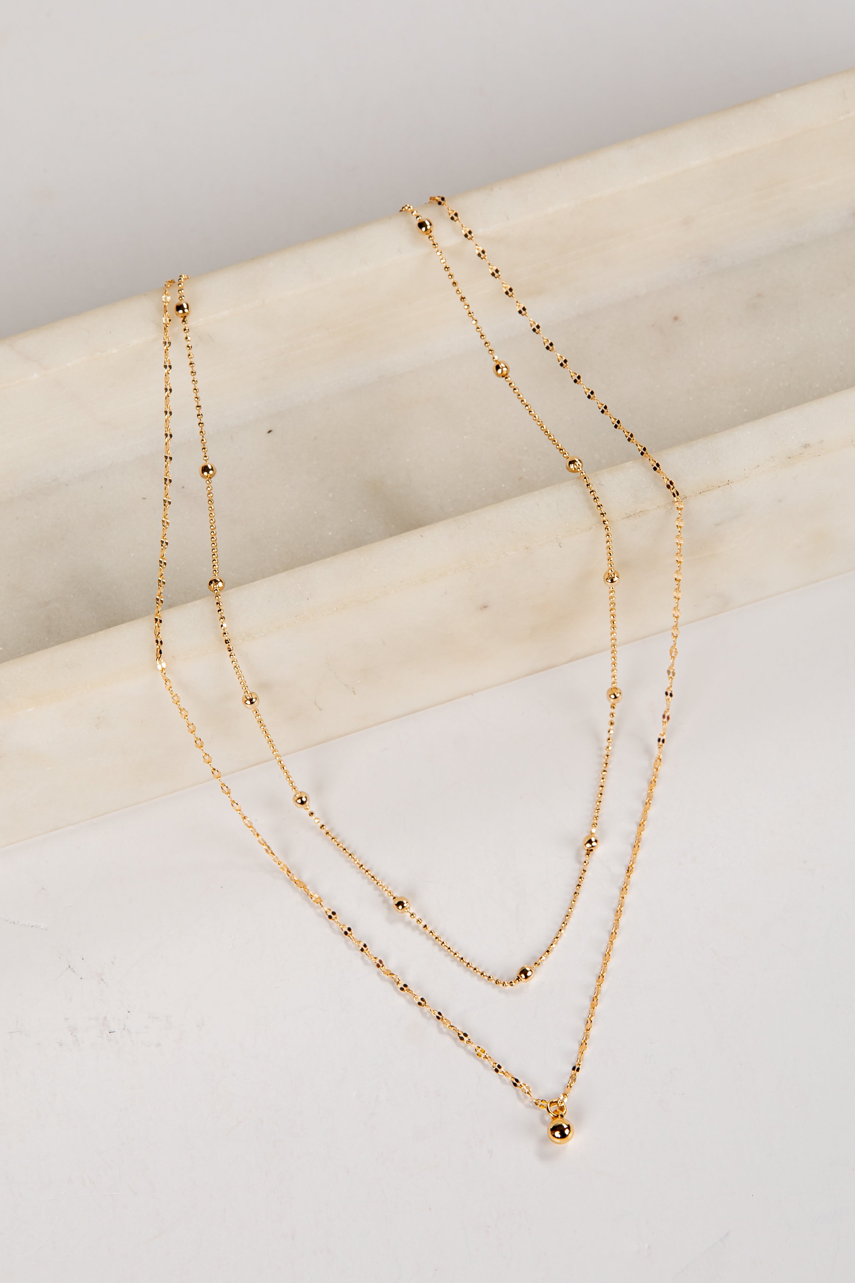 Two gold necklaces on a light wooden surface