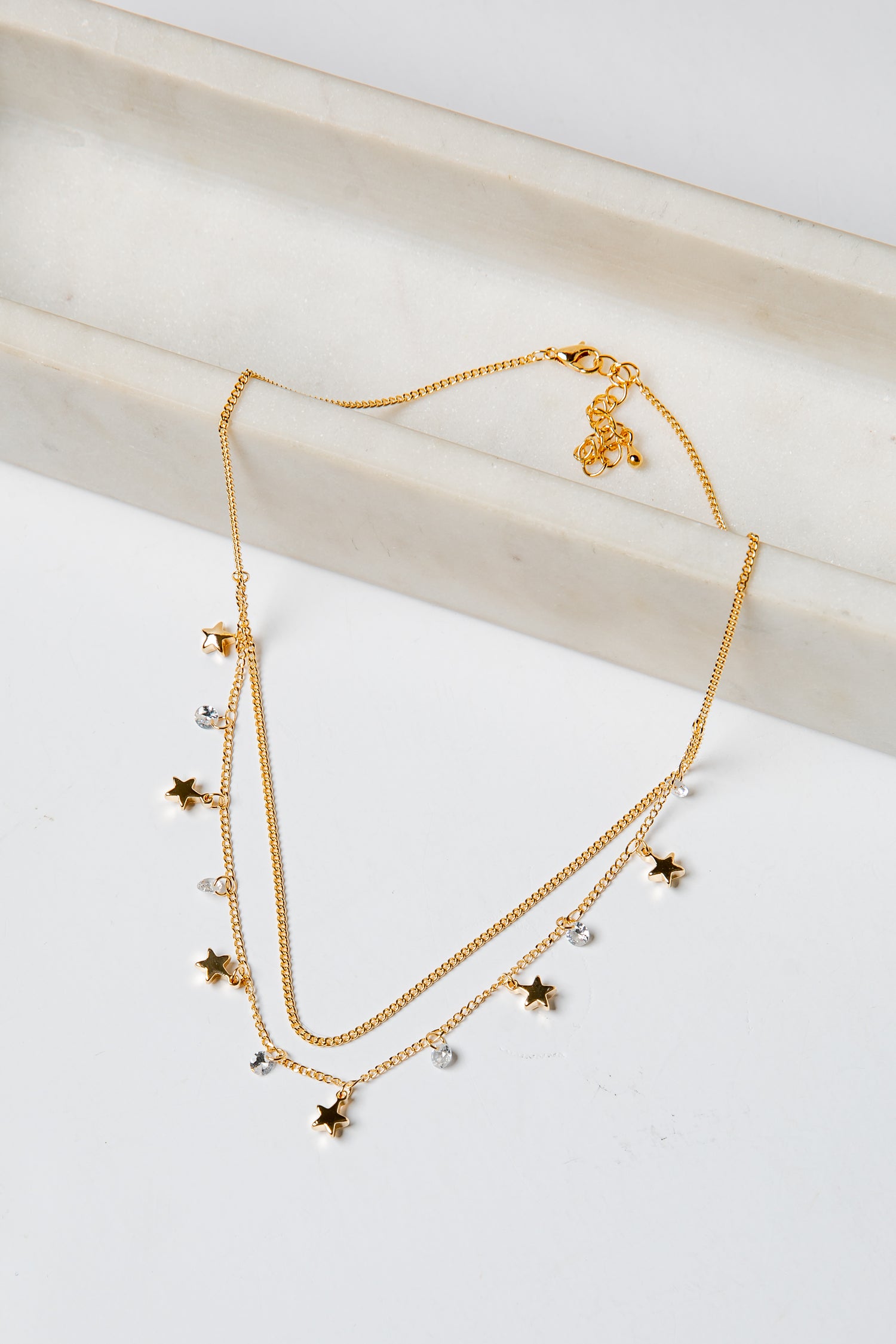 Gold layered necklace with star and heart pendants on a light background
