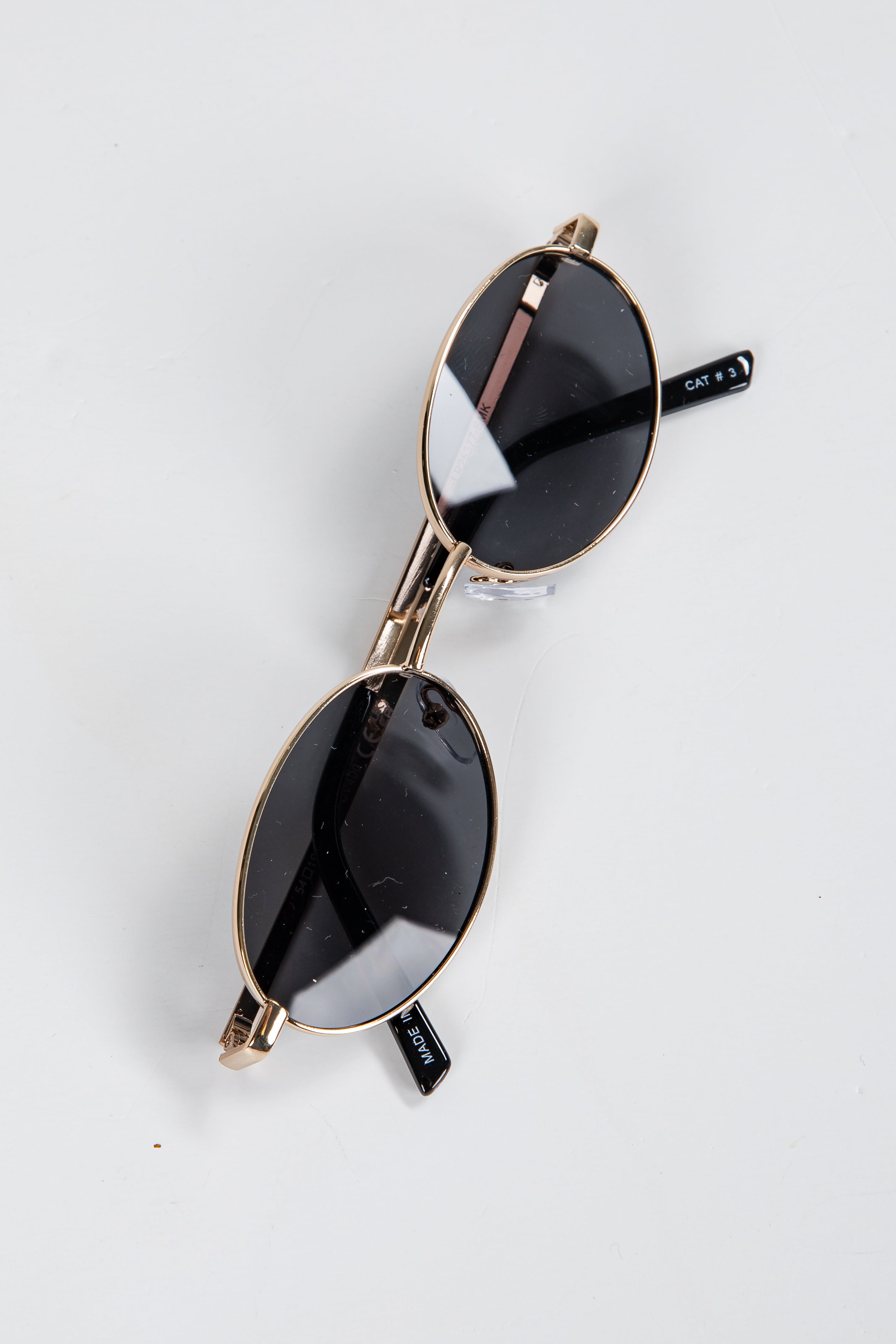 Pair of sunglasses with gold frame and black lenses on a white background