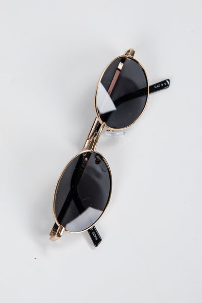 Pair of sunglasses with gold frame and black lenses on a white background