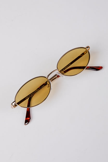 Gold-framed sunglasses with amber lenses on a light gray background