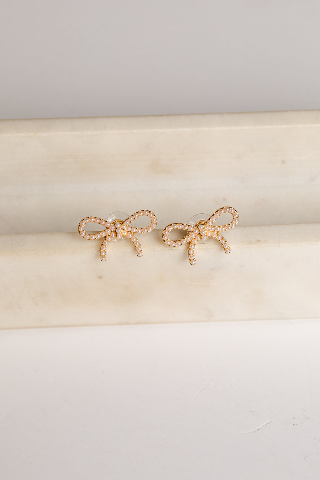 Gold bow-shaped earrings on a beige cushion with a light gray background