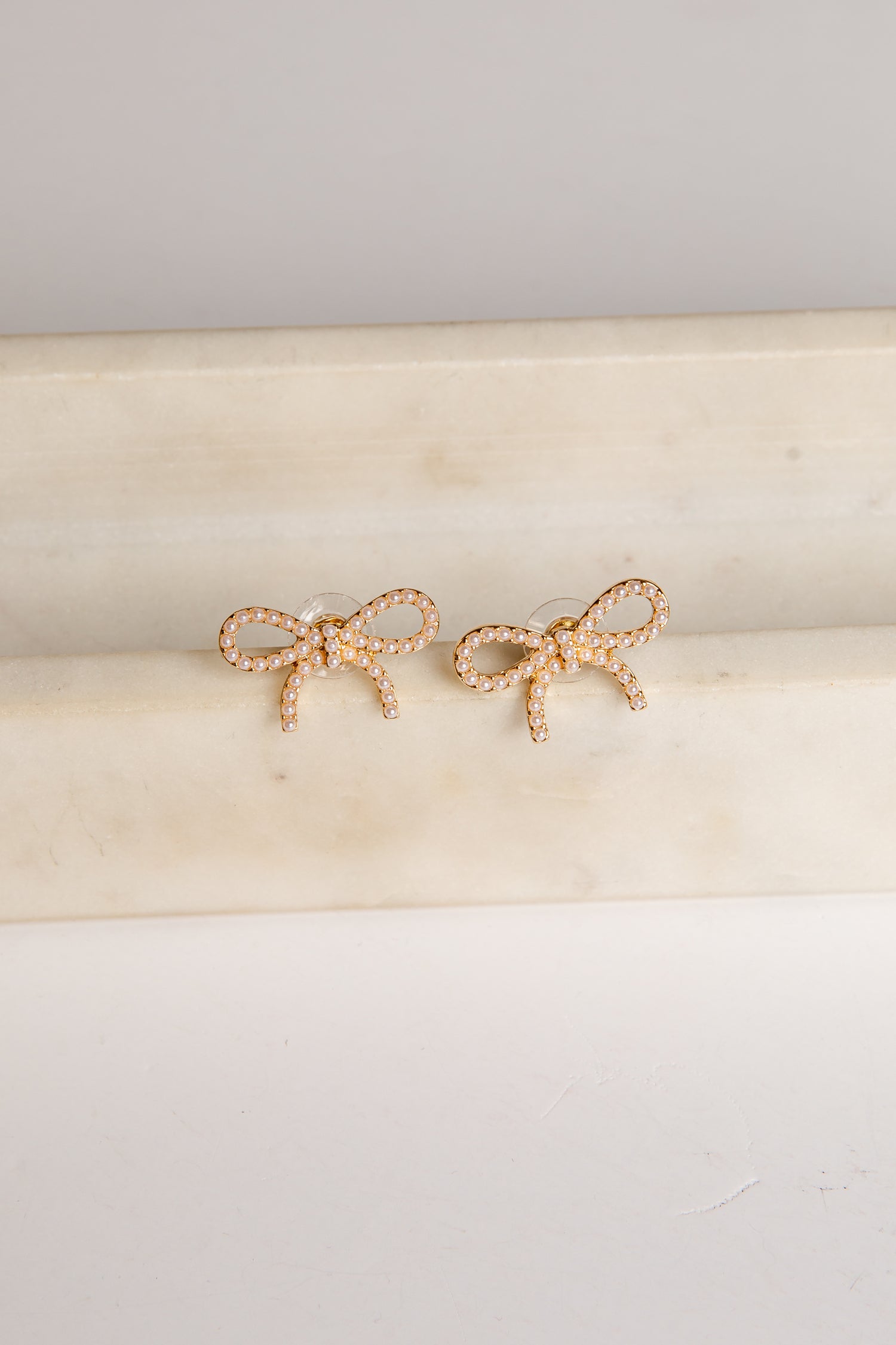 Gold bow-shaped earrings on a beige cushion with a light gray background