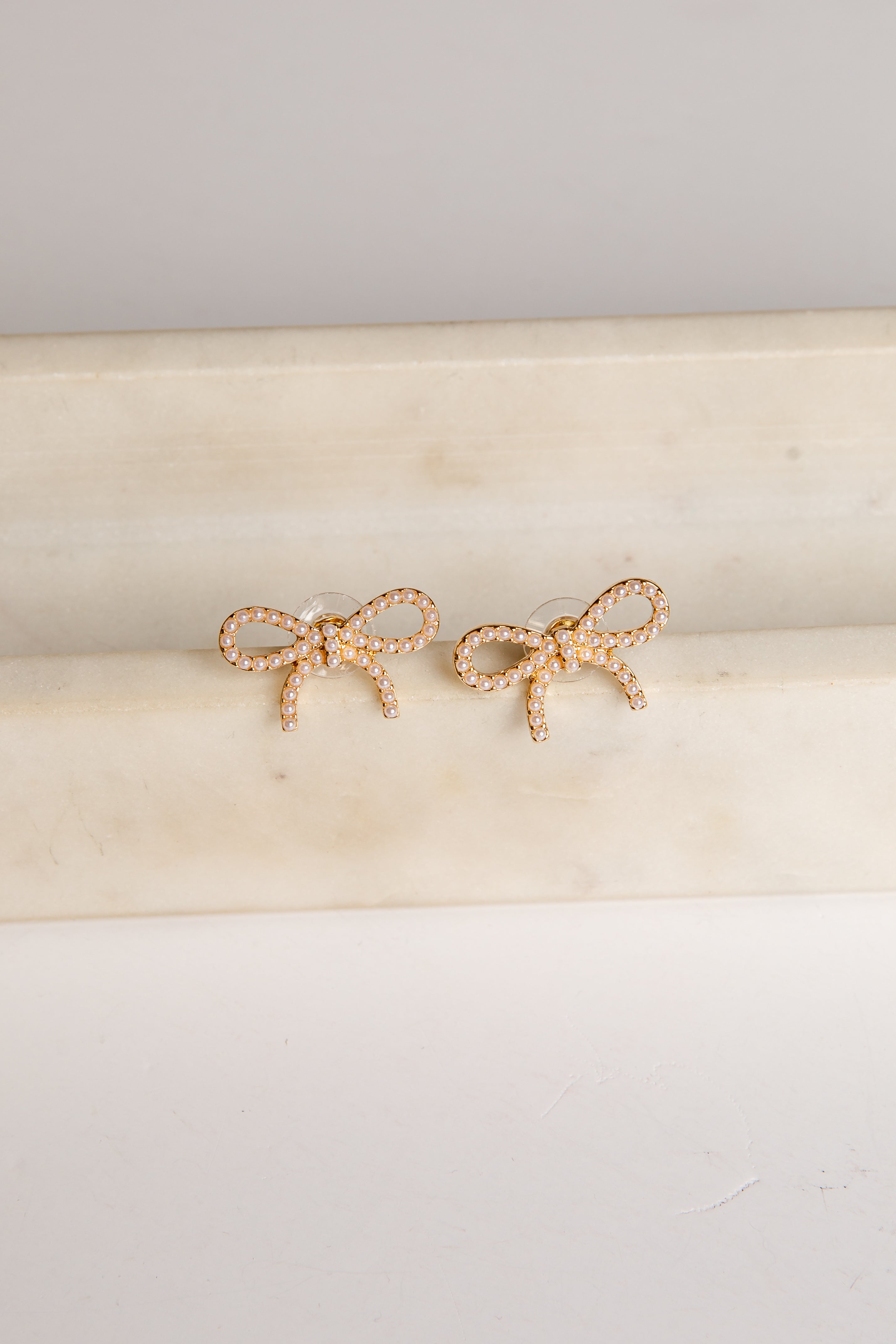 Gold bow-shaped earrings on a beige cushion with a light gray background