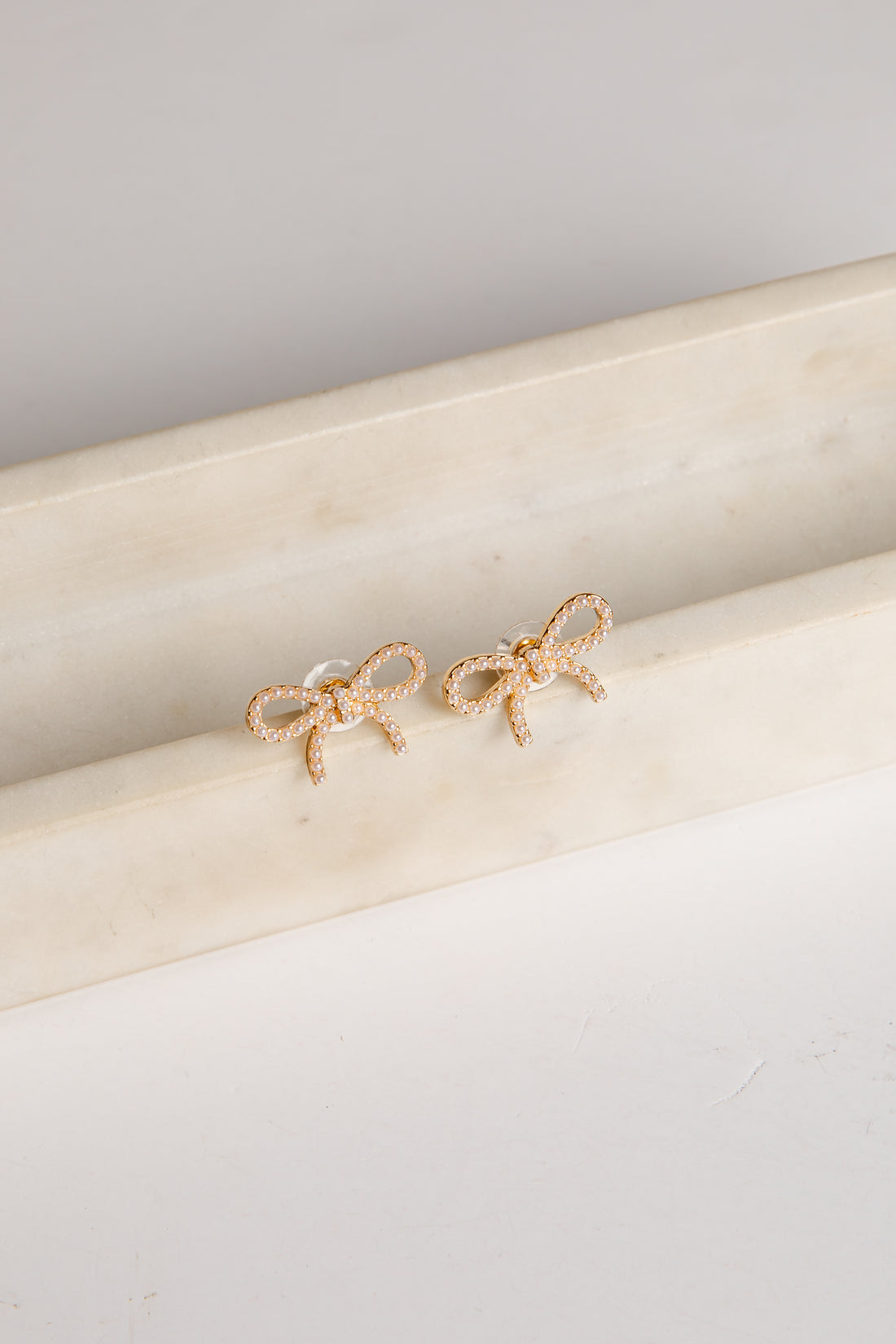 Gold bow-shaped earrings on a marble surface