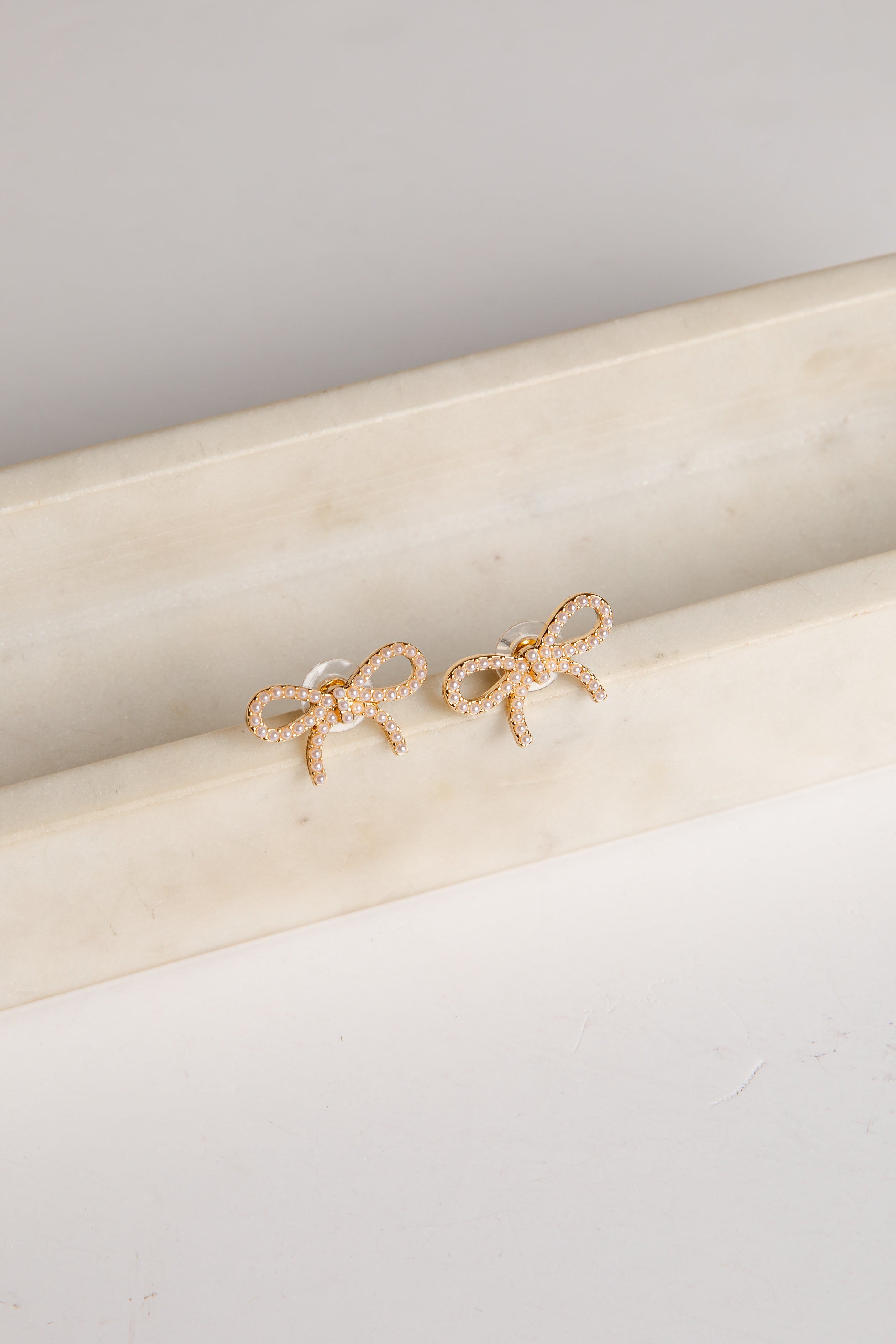 Gold bow-shaped earrings on a marble surface