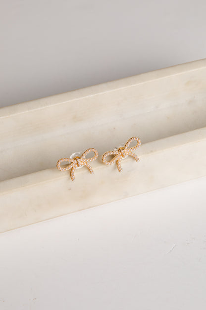 Gold bow-shaped earrings on a marble surface