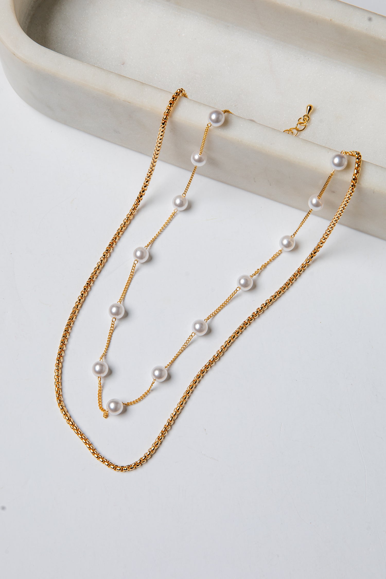 Gold necklace with pearls on a white surface