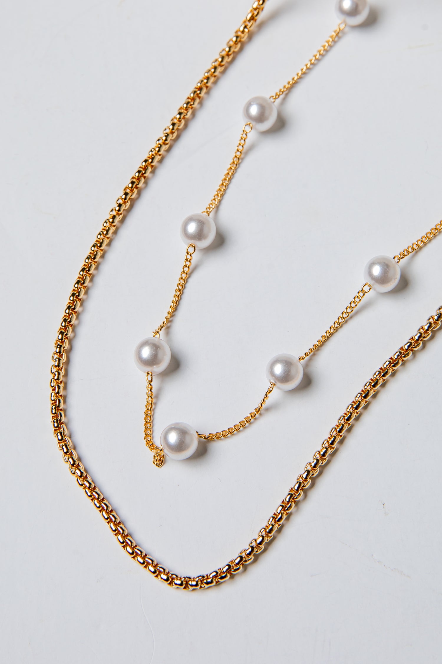 Two gold chain necklaces with pearls on a light gray background