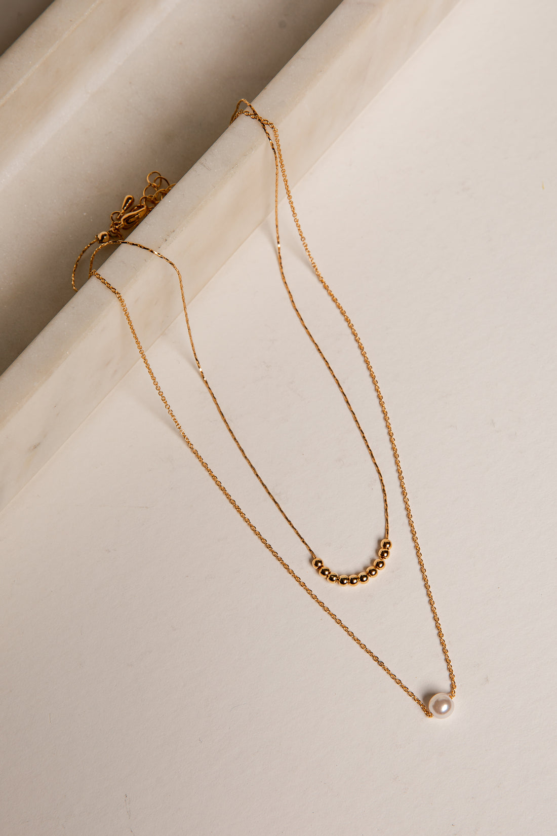 Gold necklace with a pearl pendant on a light surface