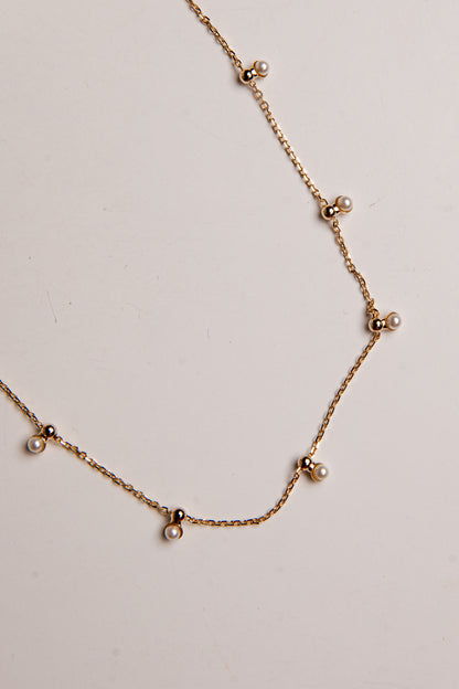A delicate gold chain necklace featuring small pearl-like beads spaced along the chain, displayed on a plain off-white background.