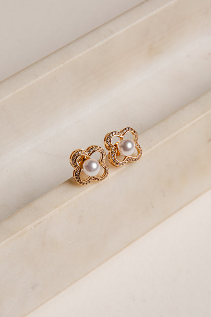 Gold earrings with pearl-like stones on a beige surface
