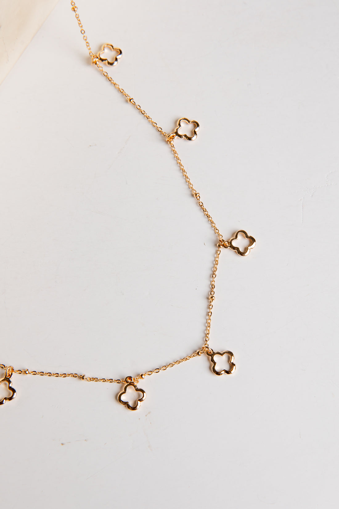 Gold necklace with clover-shaped pendants on a light gray background