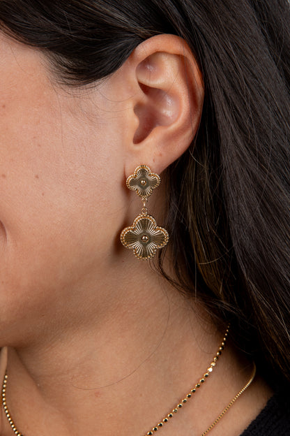 Close-up of a person wearing gold floral earrings with dark hair.