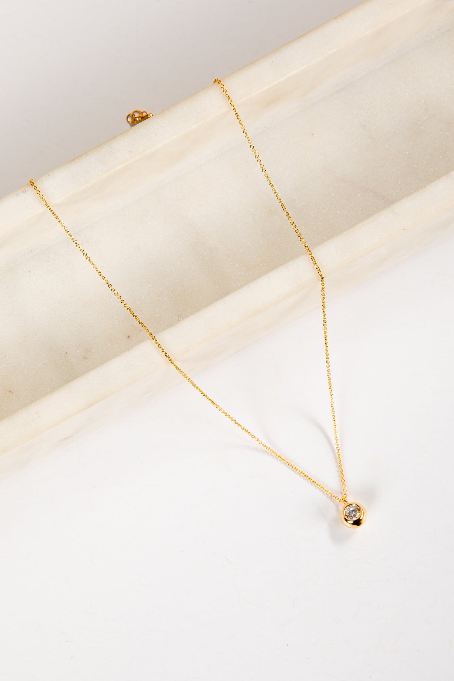 Gold necklace with a small pendant on a white surface
