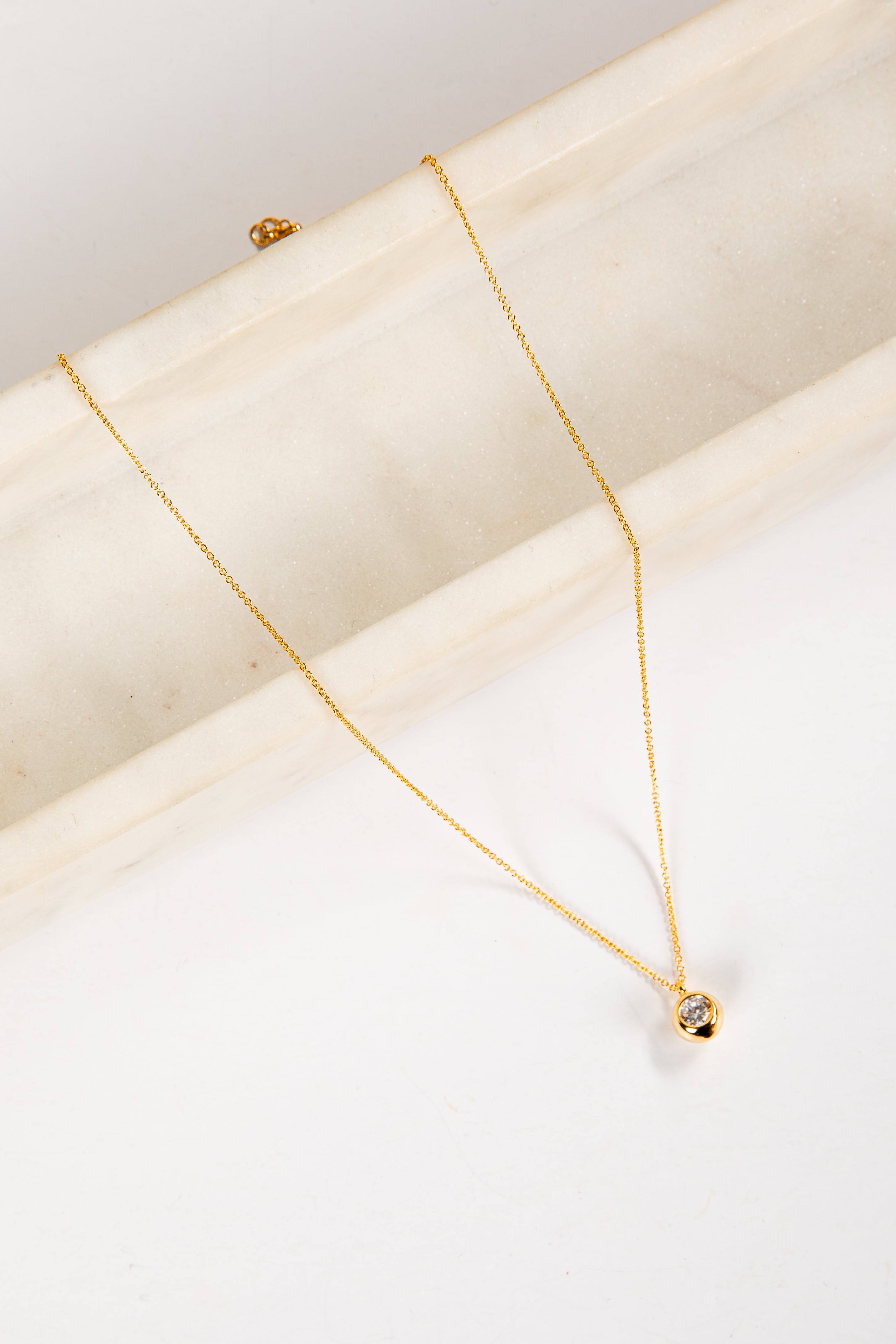 Gold necklace with a small pendant on a white surface