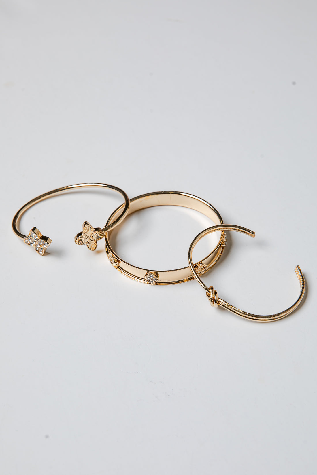 Three gold bracelets with decorative elements on a light gray background