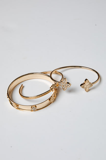 Three gold bracelets with butterfly charms on a light gray background