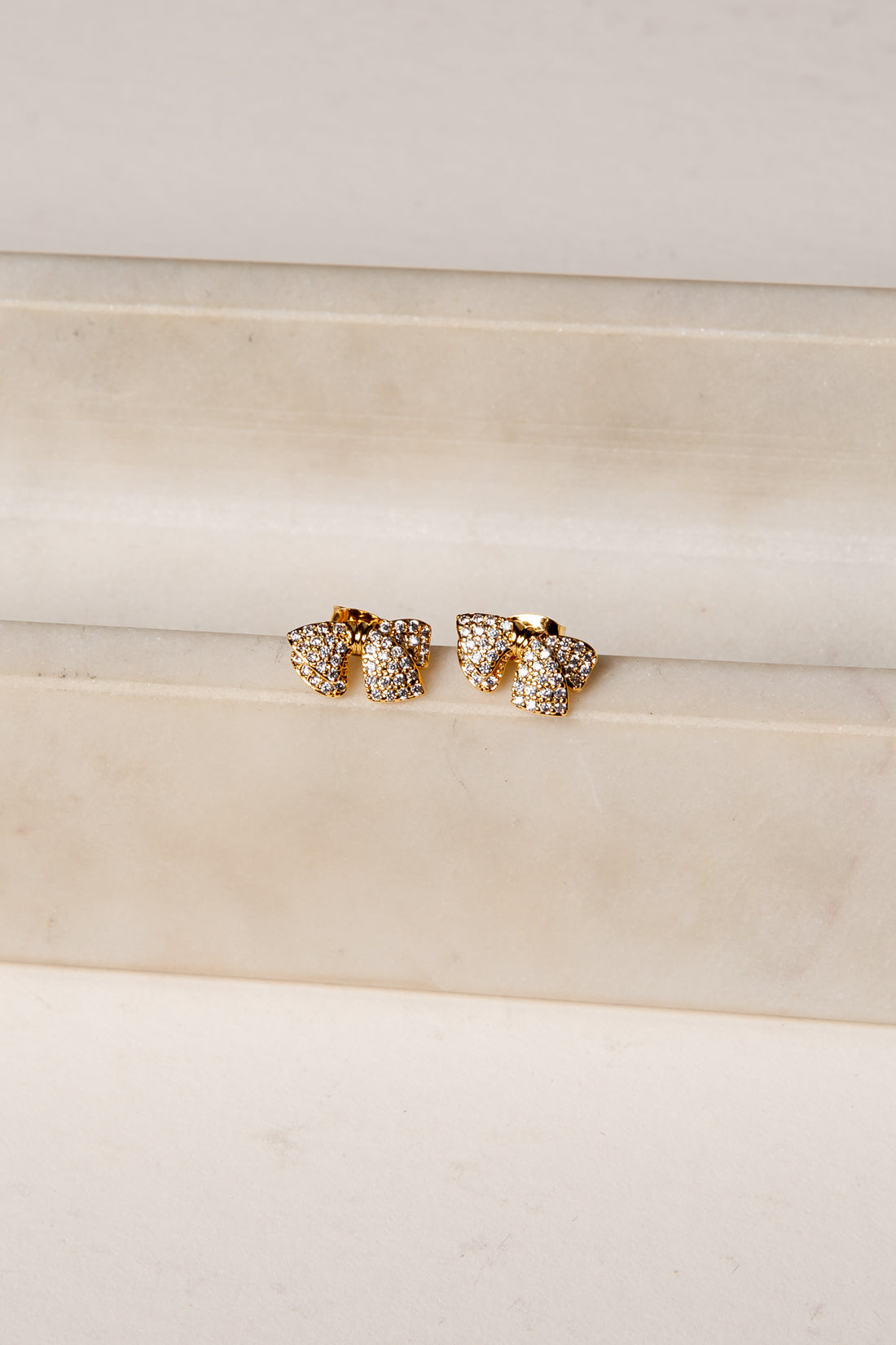 Gold earrings with clear stones on a beige fabric background