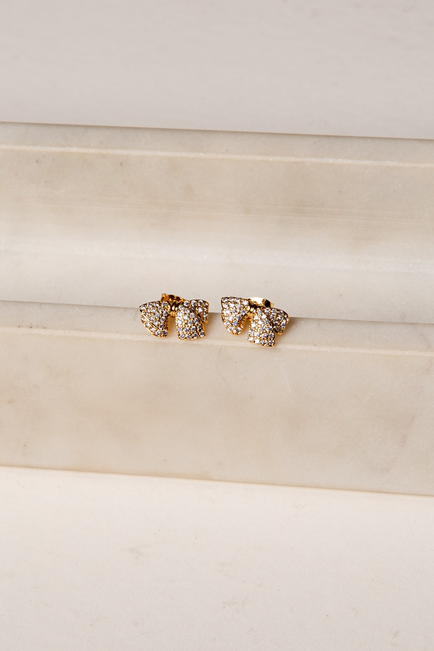Gold earrings with clear stones on a beige fabric background