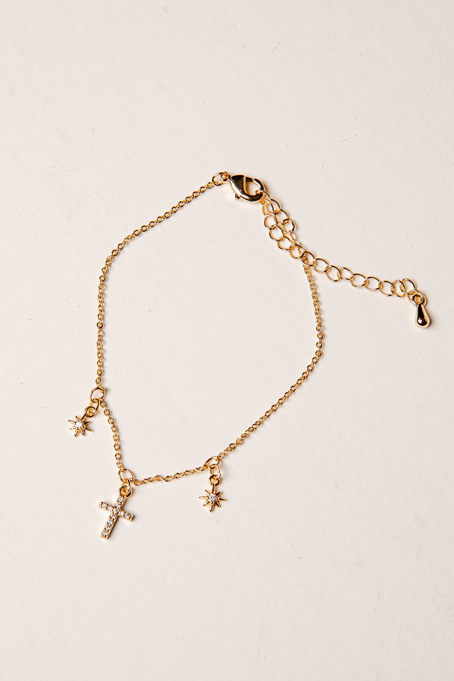 Gold bracelet with a cross and star charm on a beige background