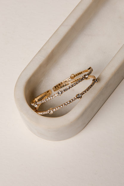 Two gold bracelets with small stones on a beige tray