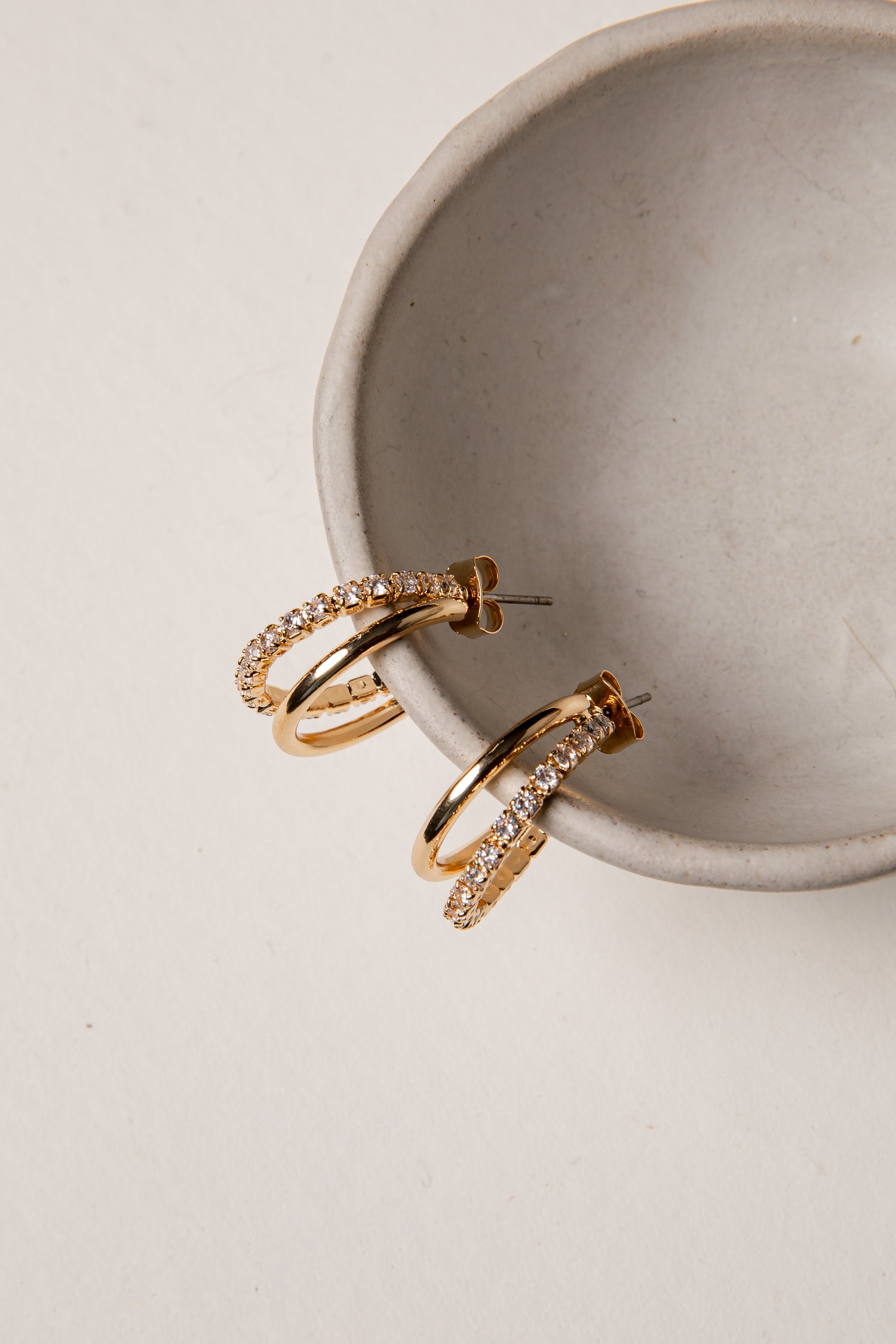 Gold hoop earrings with diamond accents on a beige surface.