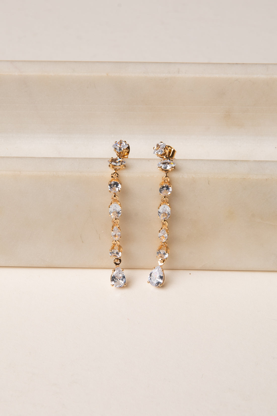 Gold and silver drop earrings on a beige surface