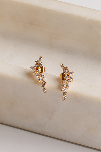 A pair of gold-toned dangle earrings with clear rhinestones, displayed on a cream-colored marble block.