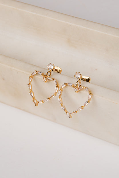 Gold heart-shaped earrings on a beige surface