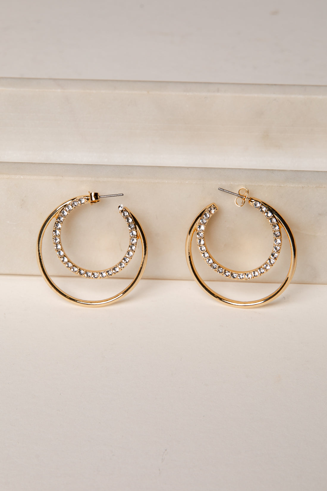 Gold hoop earrings with rhinestone detailing on a light wooden surface.