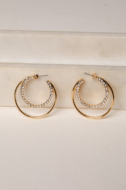 Gold hoop earrings with rhinestone detailing on a light wooden surface.