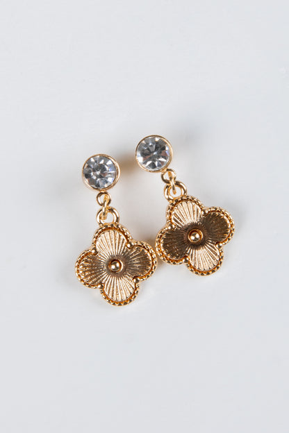 Gold floral earrings with clear gemstones on a light gray background