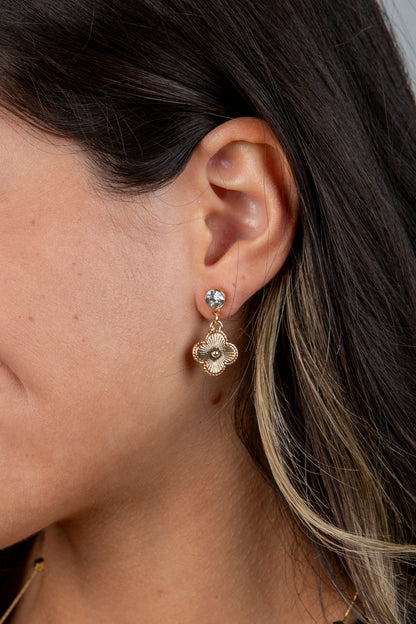 Close-up of a person wearing a gold flower-shaped earring with a clear gemstone.