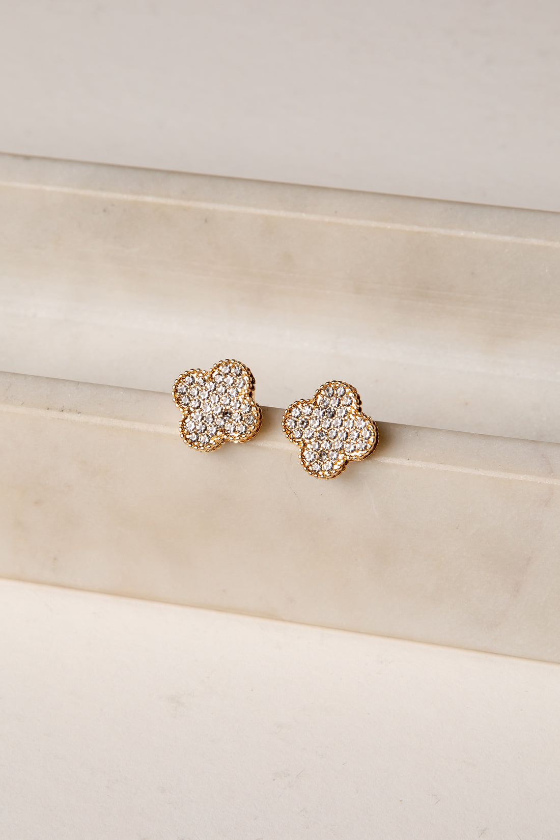 Pair of gold floral earrings with clear gemstones on a beige surface.