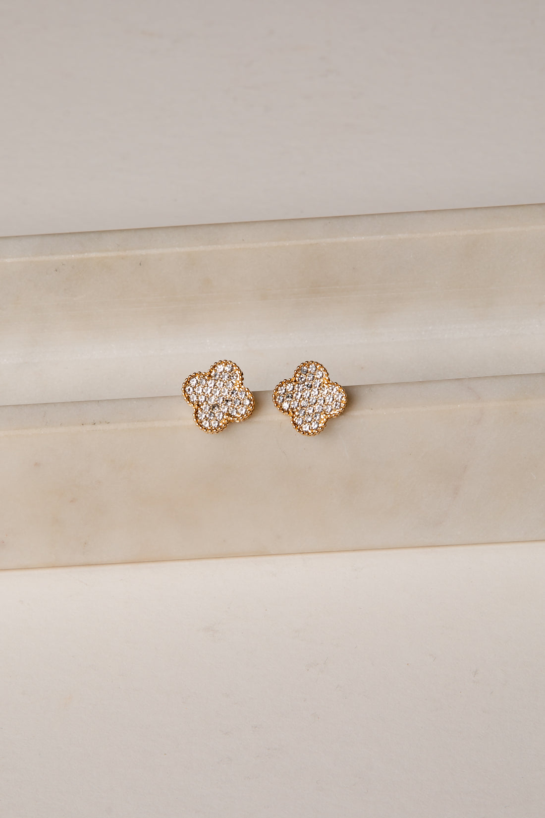 Rose gold floral earrings on a beige surface