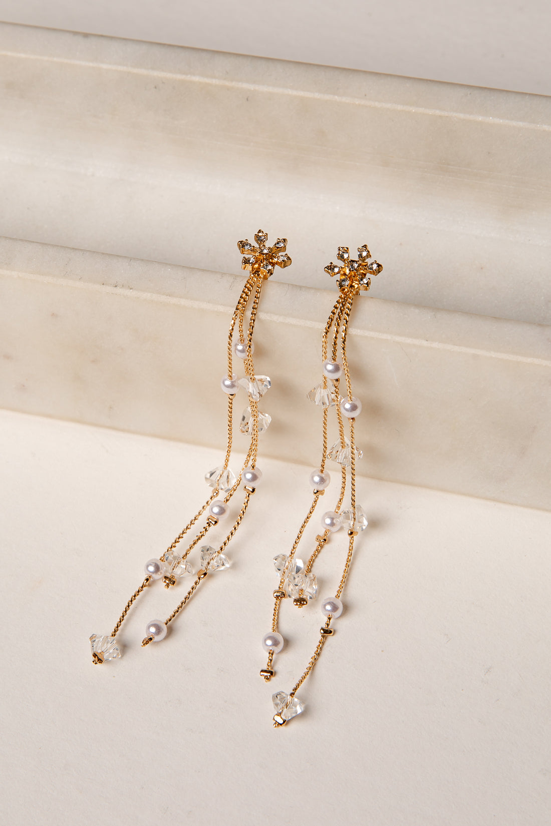 Gold and pearl earrings on a light beige surface