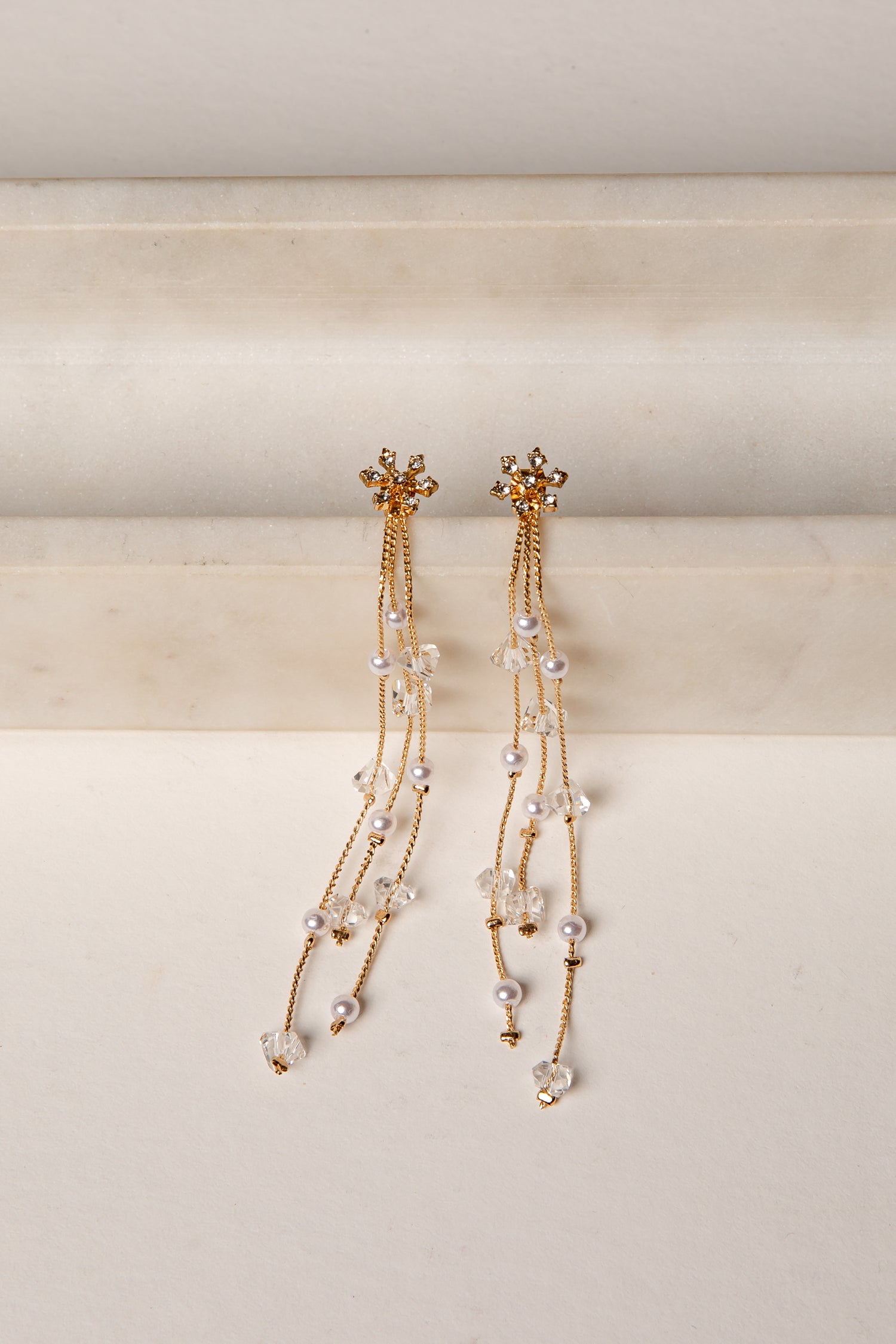 Pair of gold and pearl earrings on a beige background