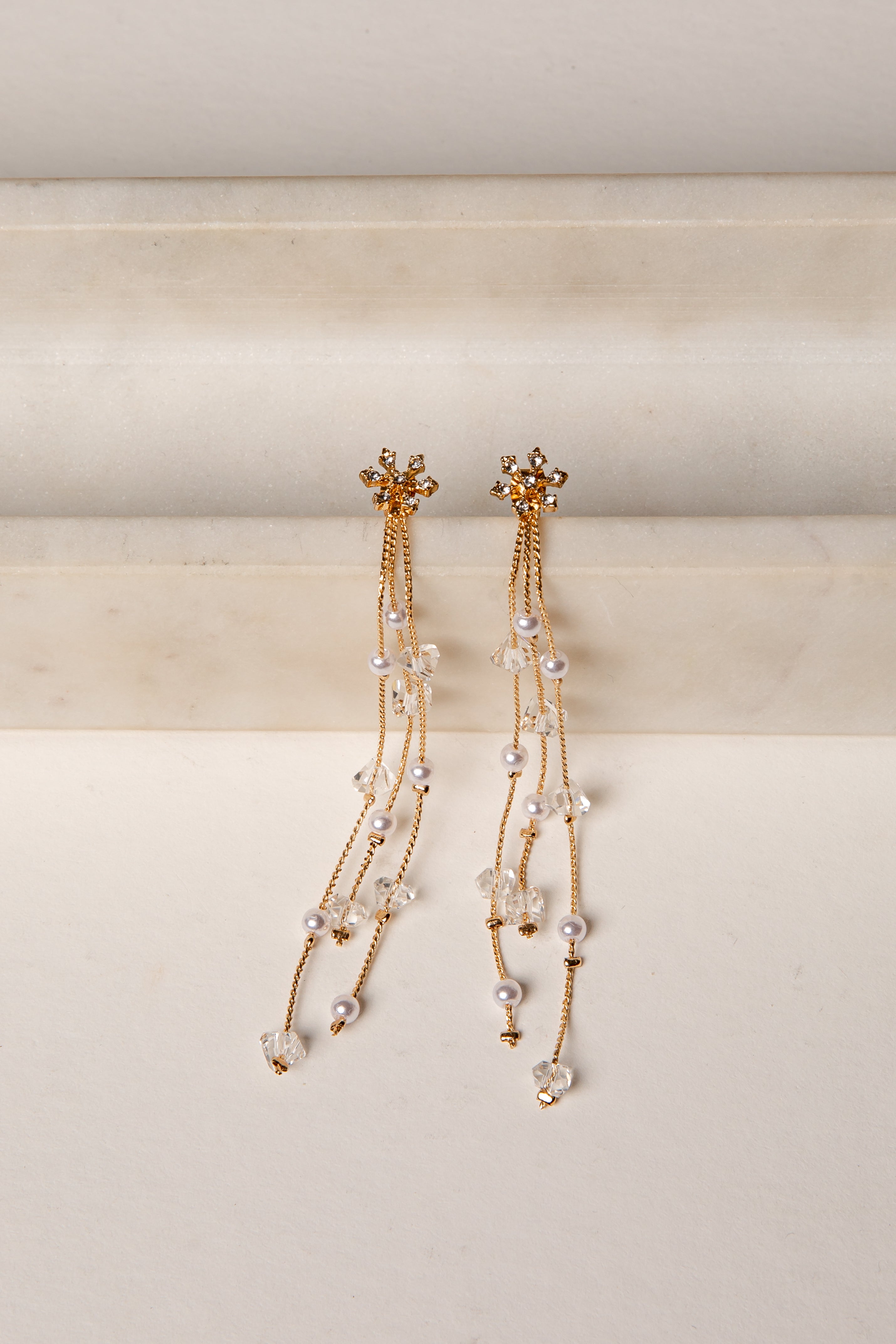 Pair of gold and pearl earrings on a beige background